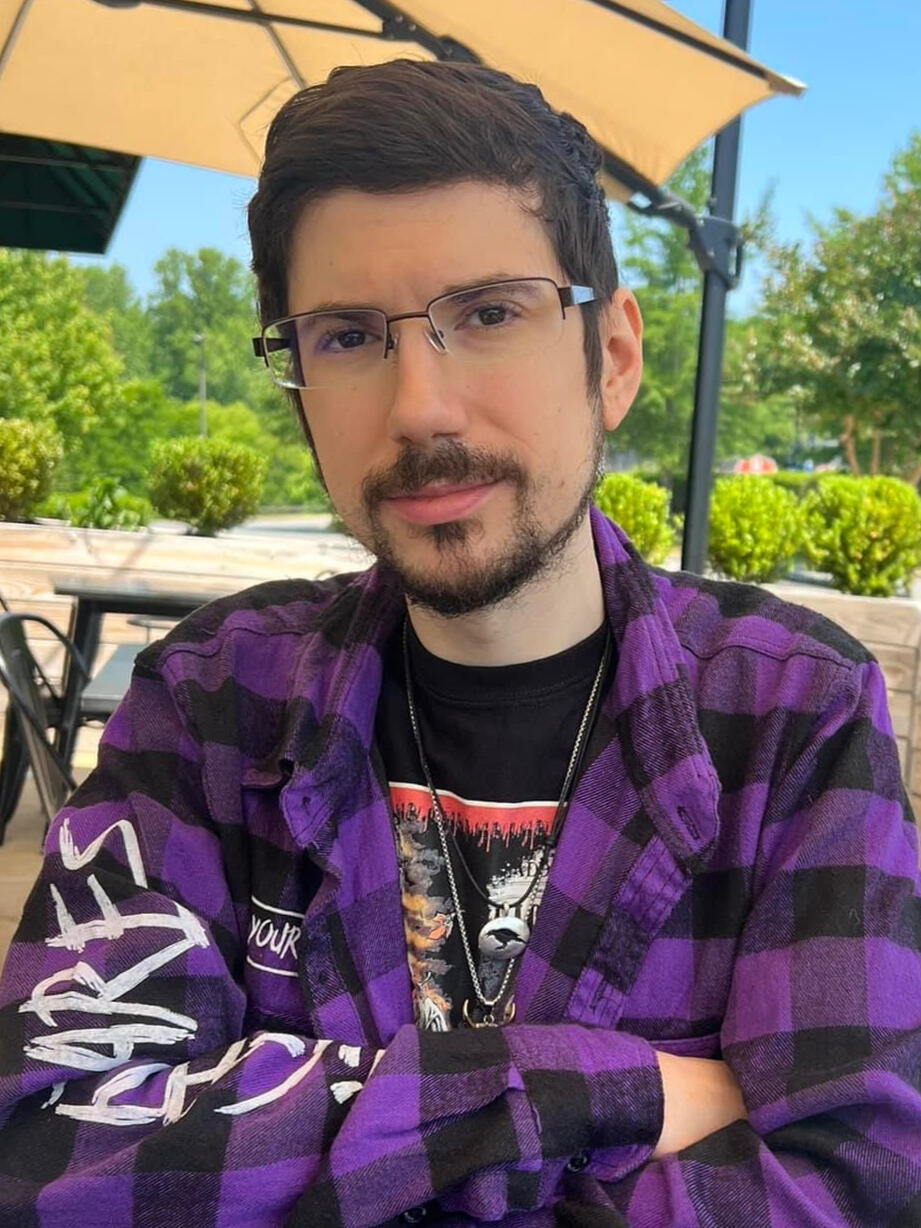 Photo of Certified Peer Support Coach Mike Cornell sitting outside, arms resting on a table, smiling at the camera.